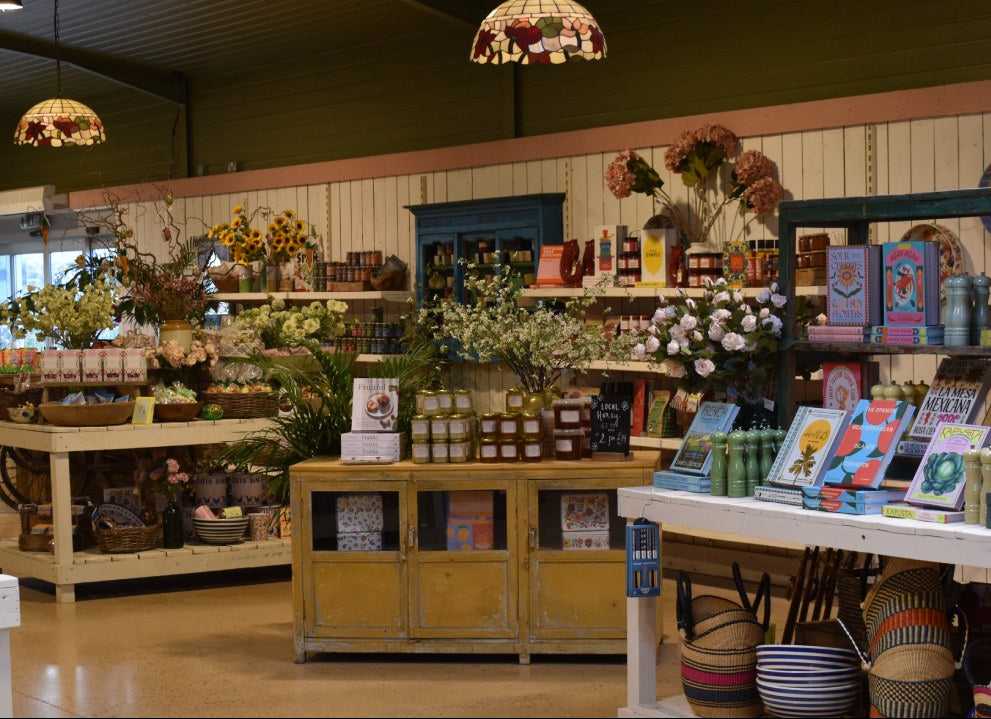 Store interior with various products on shelves and tables, including flowers and books.